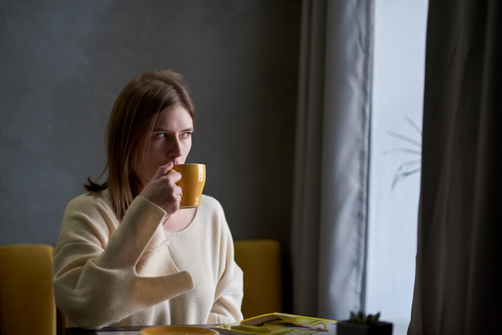 Donna-sveglia-beve-caffe Donna sveglia a tavola durante la colazione che riflette sul sonno leggero e la difficoltà di riposare profondamente